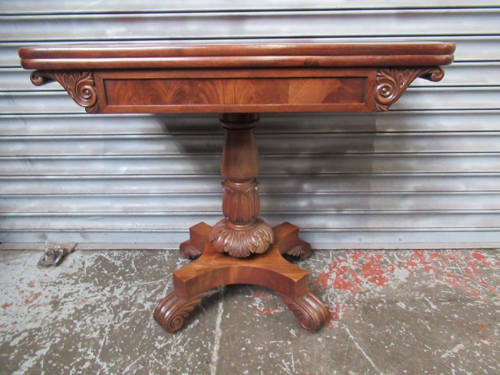 Victorian mahogany fold-over tea table featuring a rectangular swivel top, carved scroll frieze details, a central turned column, and a quadruped base with scroll feet.