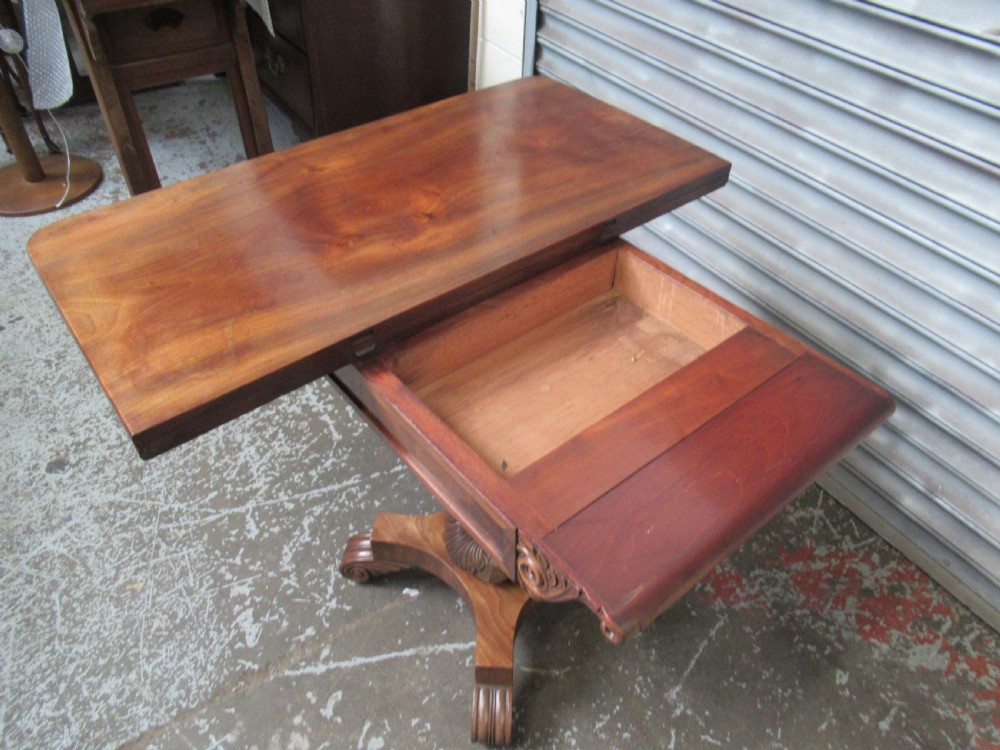 Victorian mahogany fold-over tea table featuring a rectangular swivel top, carved scroll frieze details, a central turned column, and a quadruped base with scroll feet. View IX