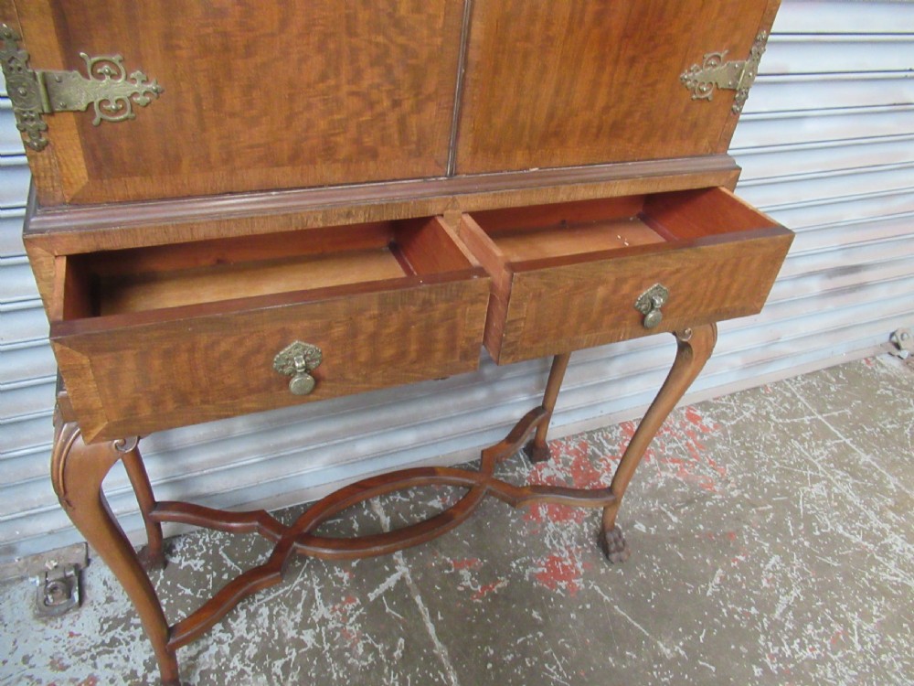 A 1930s mahogany cocktail cabinet on a stand featuring two upper doors with ornate brass strap hinges, lower drawers, cabriole legs, and claw and ball feet. View IX