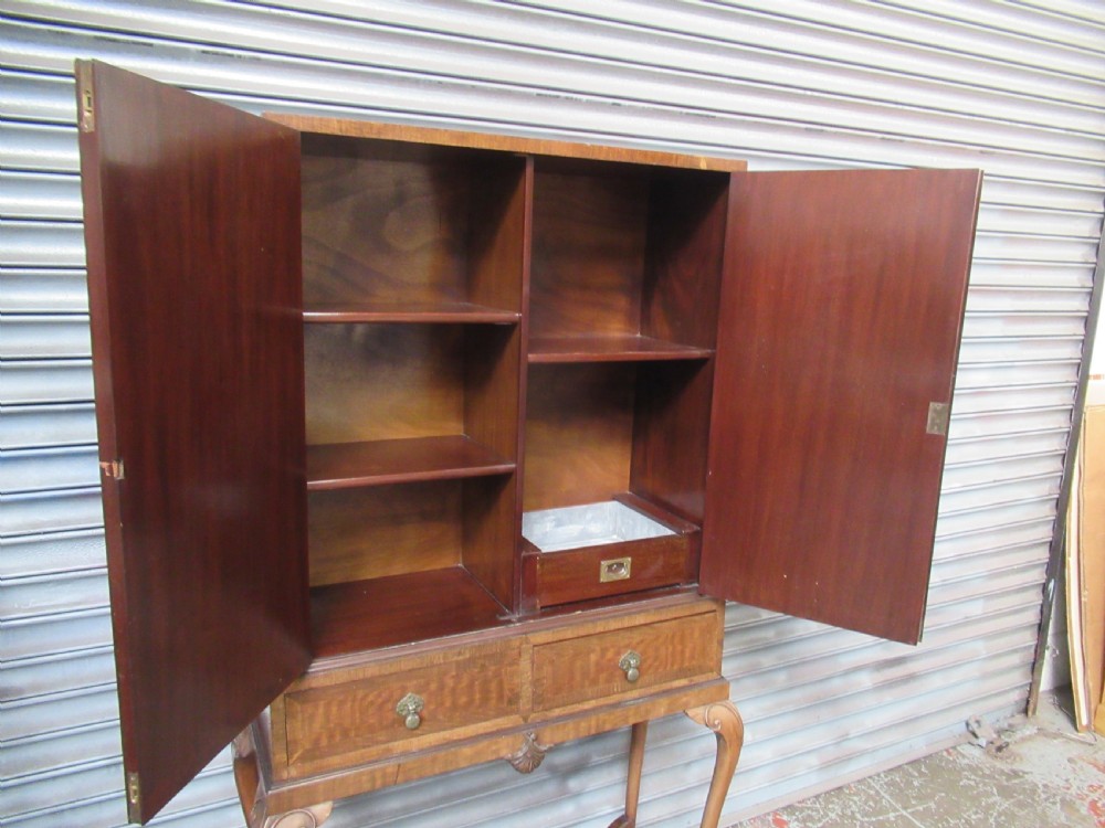 A 1930s mahogany cocktail cabinet on a stand featuring two upper doors with ornate brass strap hinges, lower drawers, cabriole legs, and claw and ball feet. View X