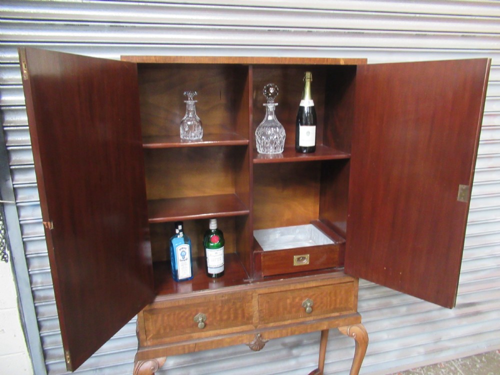 A 1930s mahogany cocktail cabinet on a stand featuring two upper doors with ornate brass strap hinges, lower drawers, cabriole legs, and claw and ball feet. View XII