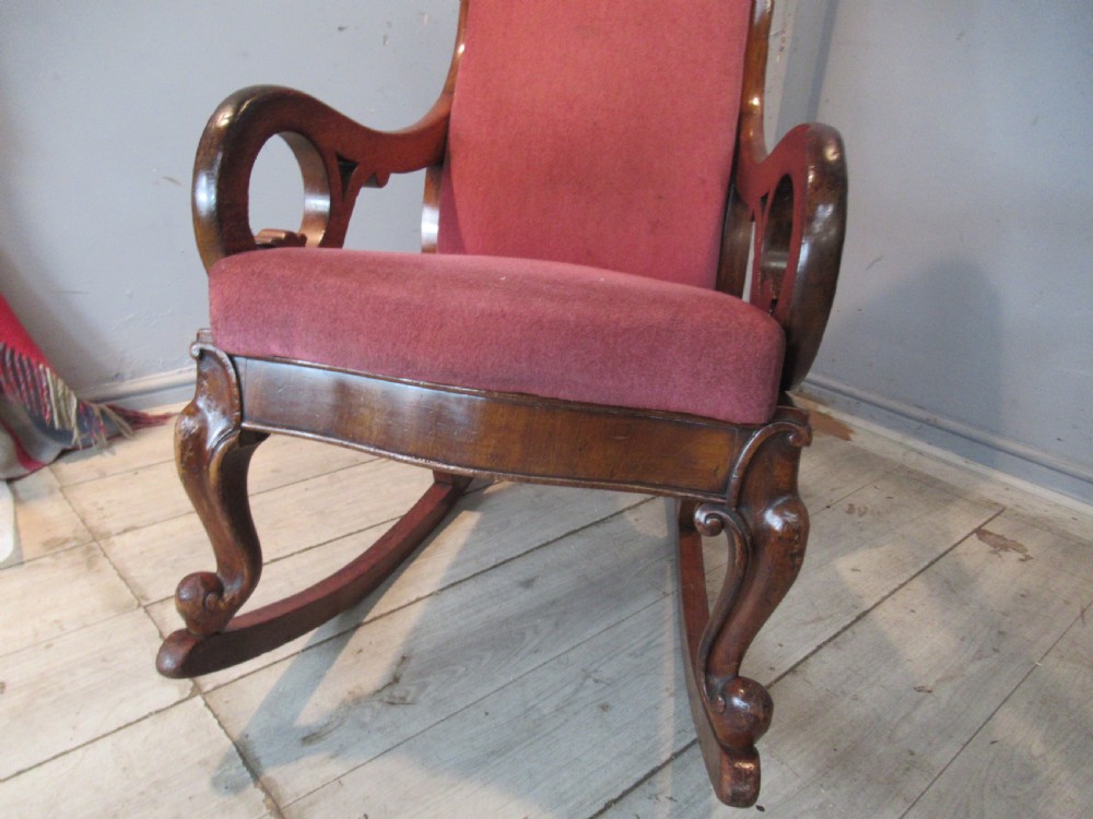 A Victorian mahogany rocking chair featuring carved scroll arms and dusty pink upholstery on curved wooden runners. View V
