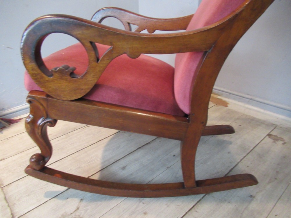 A Victorian mahogany rocking chair featuring carved scroll arms and dusty pink upholstery on curved wooden runners. View IX