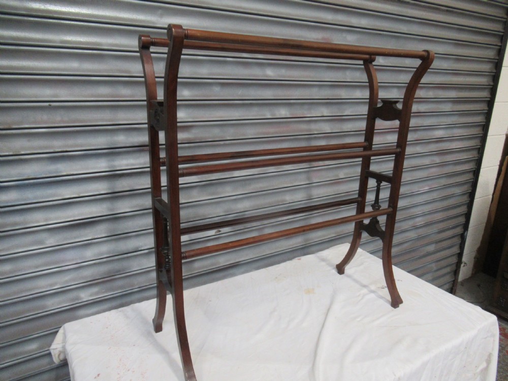 An Edwardian freestanding mahogany towel rail featuring curved top rail supports, carved rosette side mounts, turned central spindles, and splayed feet. View II