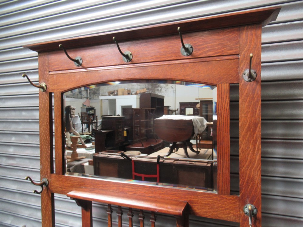 A tall Edwardian oak hall stand featuring an upper mirror, brass hanging hooks, a central glove box shelf, and a lower umbrella stand with metal drip trays. View II