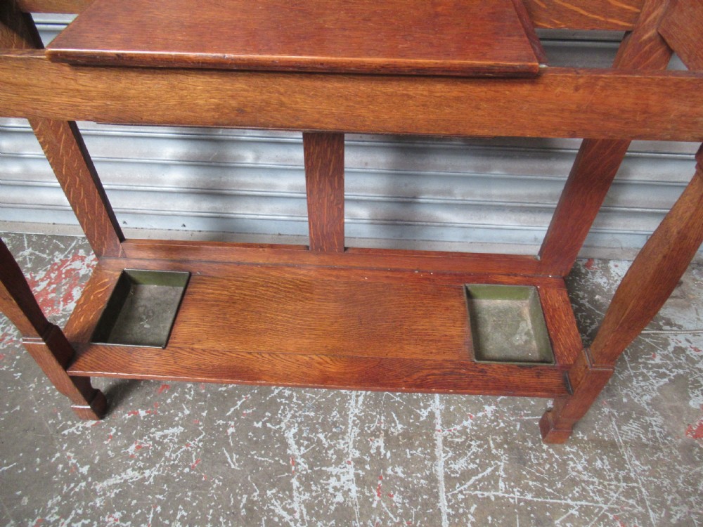 A tall Edwardian oak hall stand featuring an upper mirror, brass hanging hooks, a central glove box shelf, and a lower umbrella stand with metal drip trays. View VII
