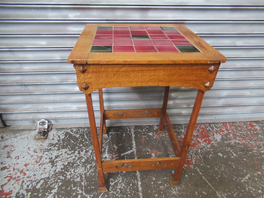 An Arts and Crafts oak side table with a square red and green glazed ceramic tile top, raised on splayed legs with pierced stretchers. View VII
