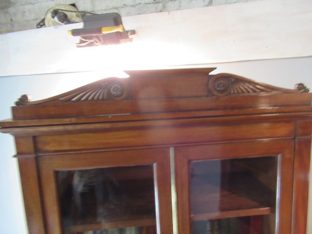 An early nineteenth-century mahogany glazed cupboard bookcase featuring a carved pediment top, two upper glass doors, and two lower panelled cupboard doors with diamond veneer details. View III