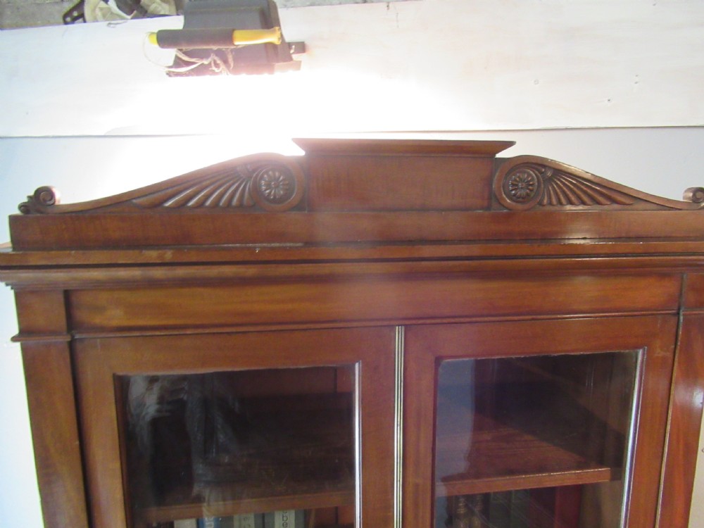 An early nineteenth-century mahogany glazed cupboard bookcase featuring a carved pediment top, two upper glass doors, and two lower panelled cupboard doors with diamond veneer details. View IV