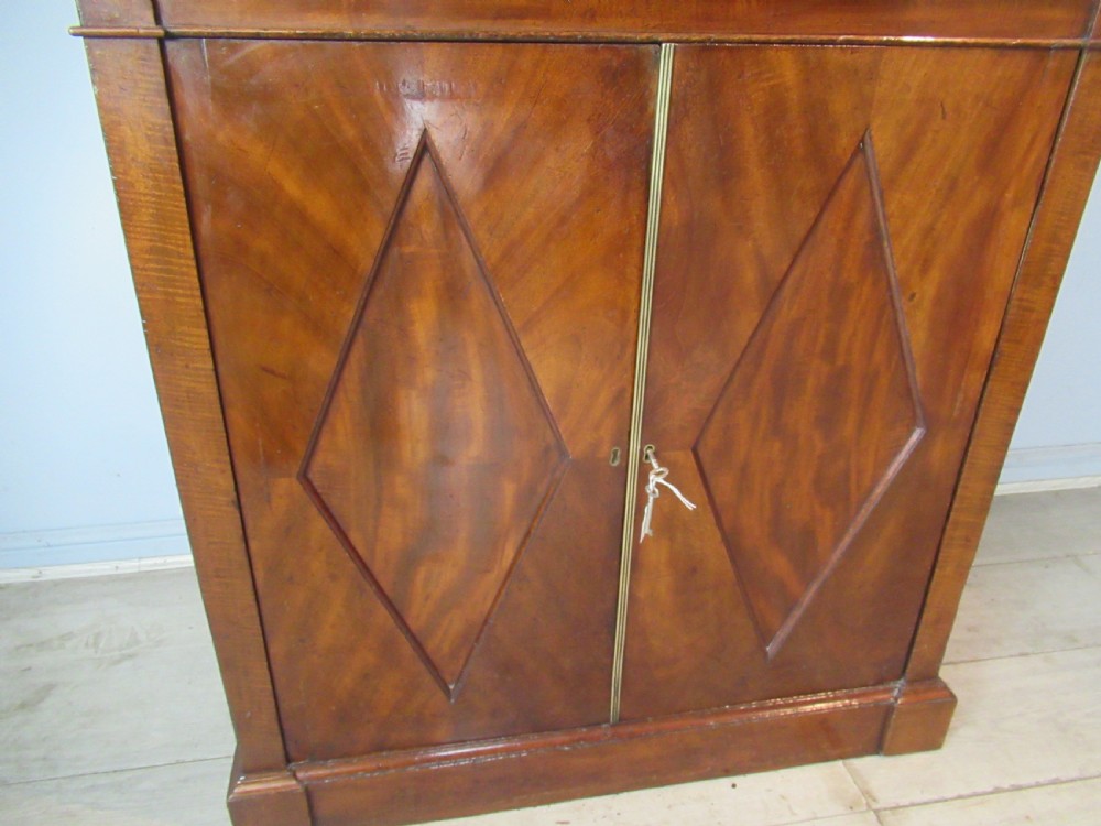 An early nineteenth-century mahogany glazed cupboard bookcase featuring a carved pediment top, two upper glass doors, and two lower panelled cupboard doors with diamond veneer details. View XII