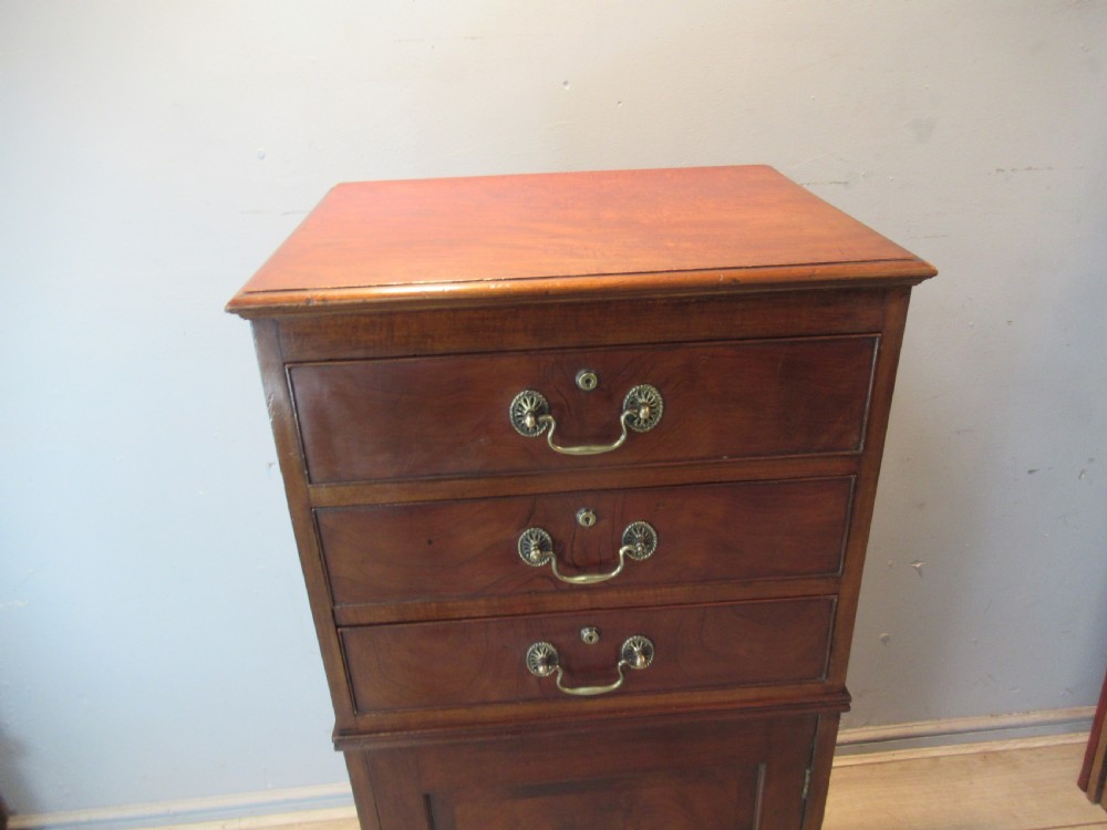 A tall, slim Victorian mahogany cabinet featuring three upper drawers with brass handles above a single lower cupboard door. View VI