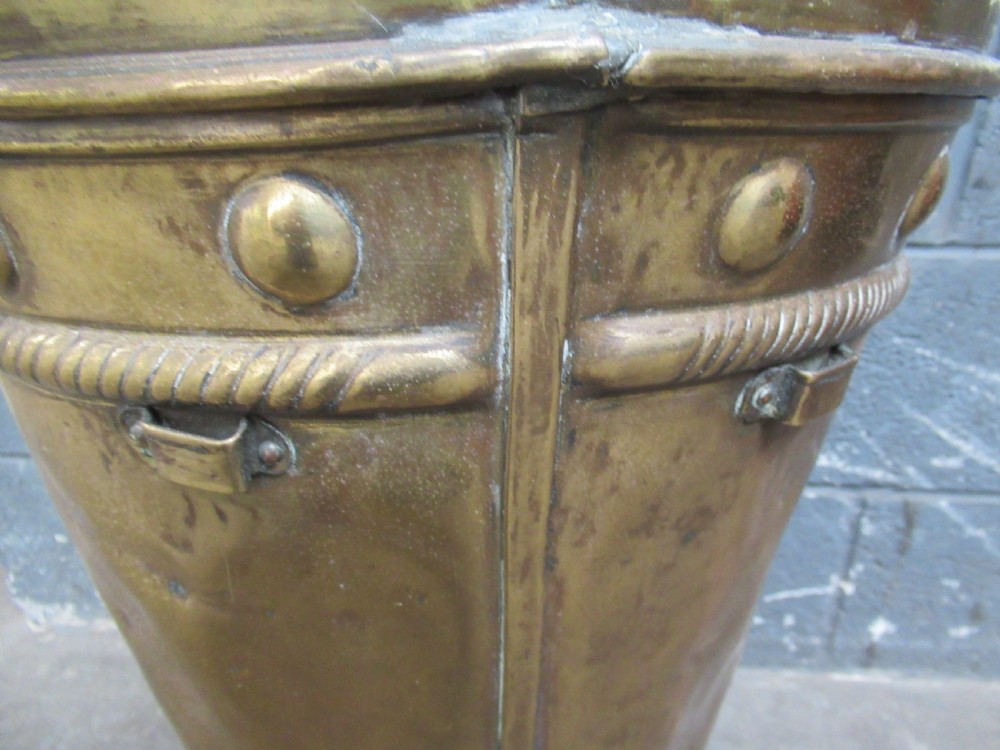 A tall, tapered brass stick stand featuring embossed relief scenes of tavern figures, decorative studding, and a raised back rim. View X