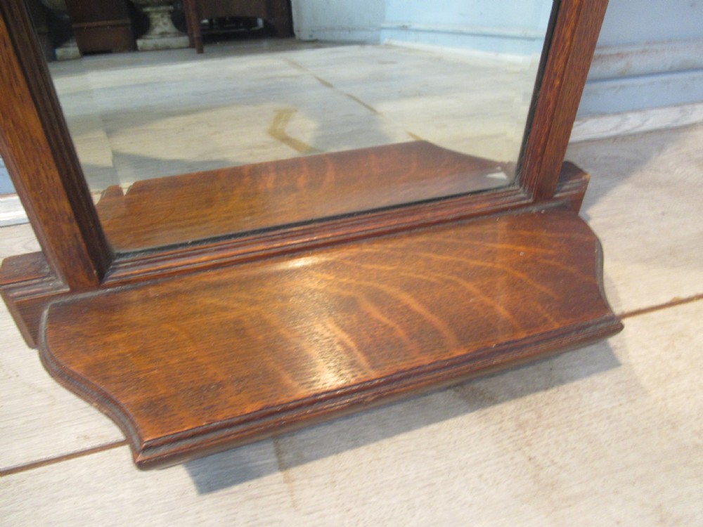A late Victorian oak framed wall mirror featuring top brass corner mounts and an integrated lower shelf. View V