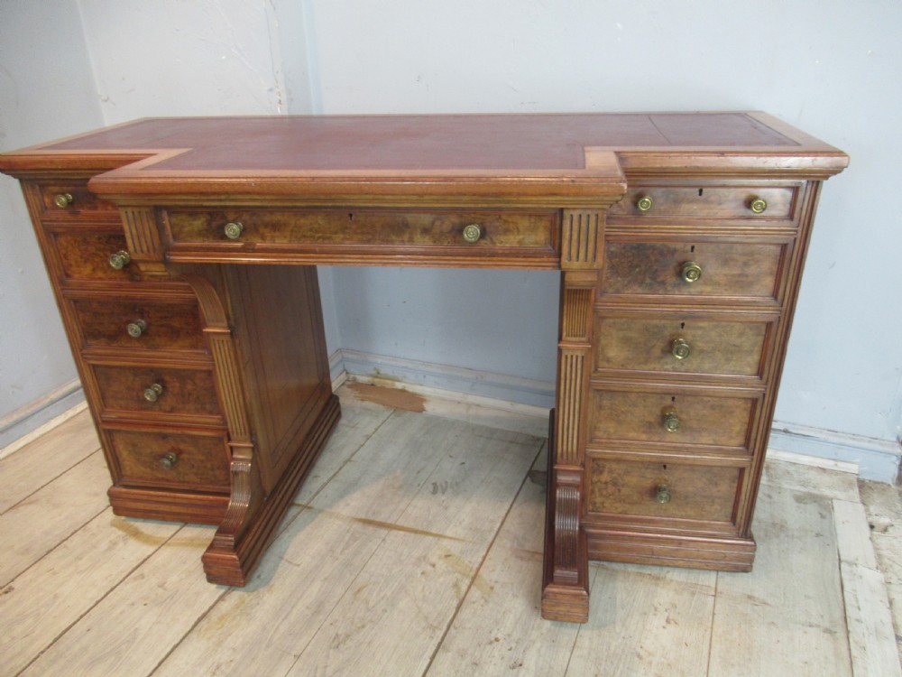 A late Victorian walnut pedestal desk featuring a dark leather writing inset, multiple burr walnut drawer fronts with brass knobs, and fluted column accents. View II