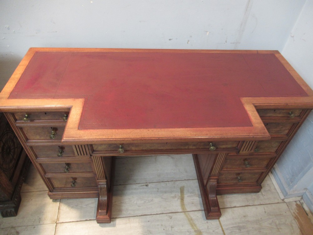 A late Victorian walnut pedestal desk featuring a dark leather writing inset, multiple burr walnut drawer fronts with brass knobs, and fluted column accents. View XI