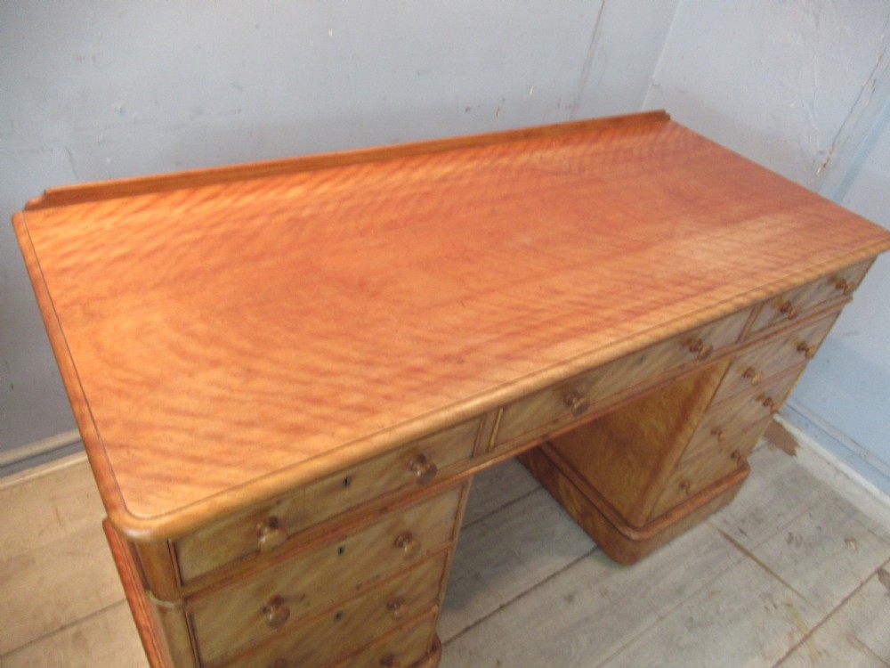 A Victorian satin birch kneehole desk featuring nine drawers with turned wooden handles and a solid plinth base. View V