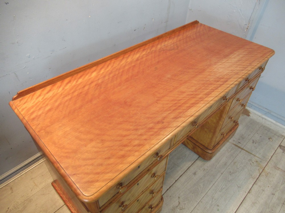 A Victorian satin birch kneehole desk featuring nine drawers with turned wooden handles and a solid plinth base. View VI
