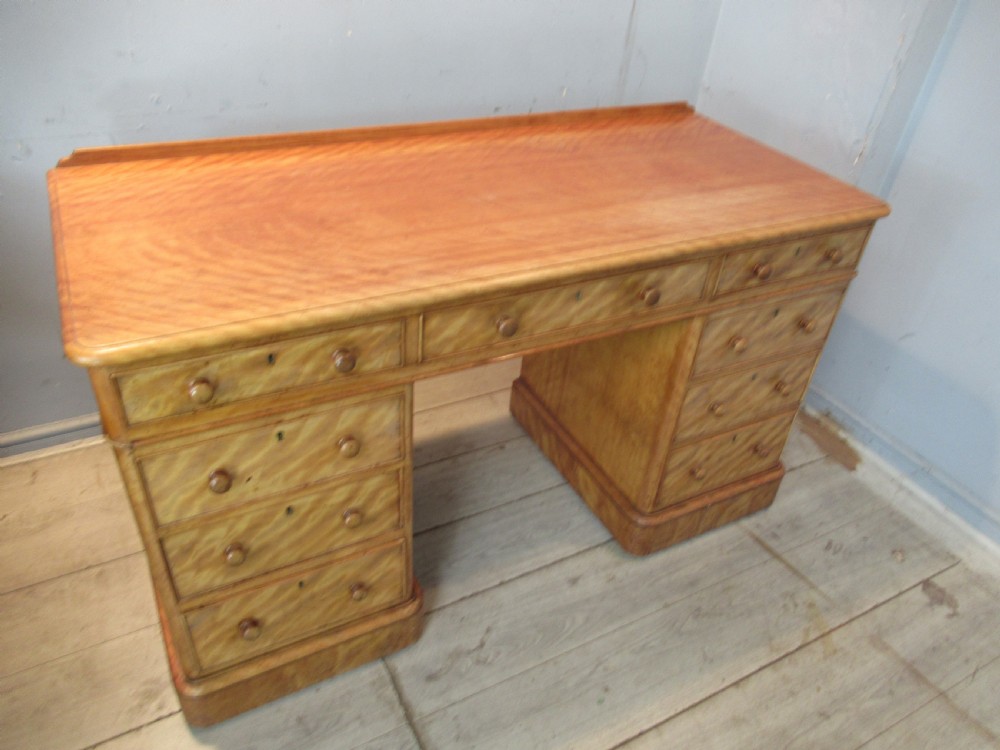 A Victorian satin birch kneehole desk featuring nine drawers with turned wooden handles and a solid plinth base. View XI