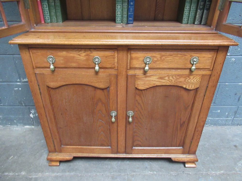 A 1920s warm brown oak cupboard bookcase featuring two upper glazed doors with geometric astragal glazing, two drawers, and a two-door lower cupboard. View V