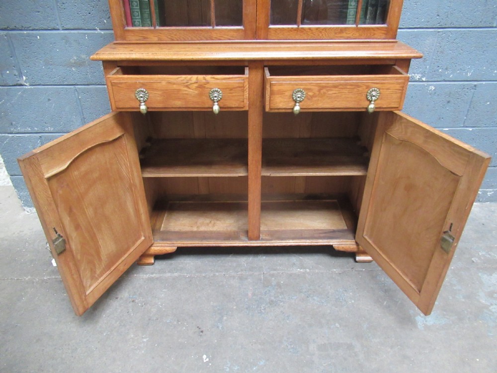 A 1920s warm brown oak cupboard bookcase featuring two upper glazed doors with geometric astragal glazing, two drawers, and a two-door lower cupboard. View X