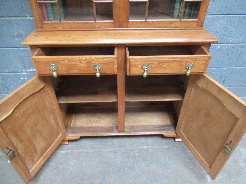 A 1920s warm brown oak cupboard bookcase featuring two upper glazed doors with geometric astragal glazing, two drawers, and a two-door lower cupboard. View XI