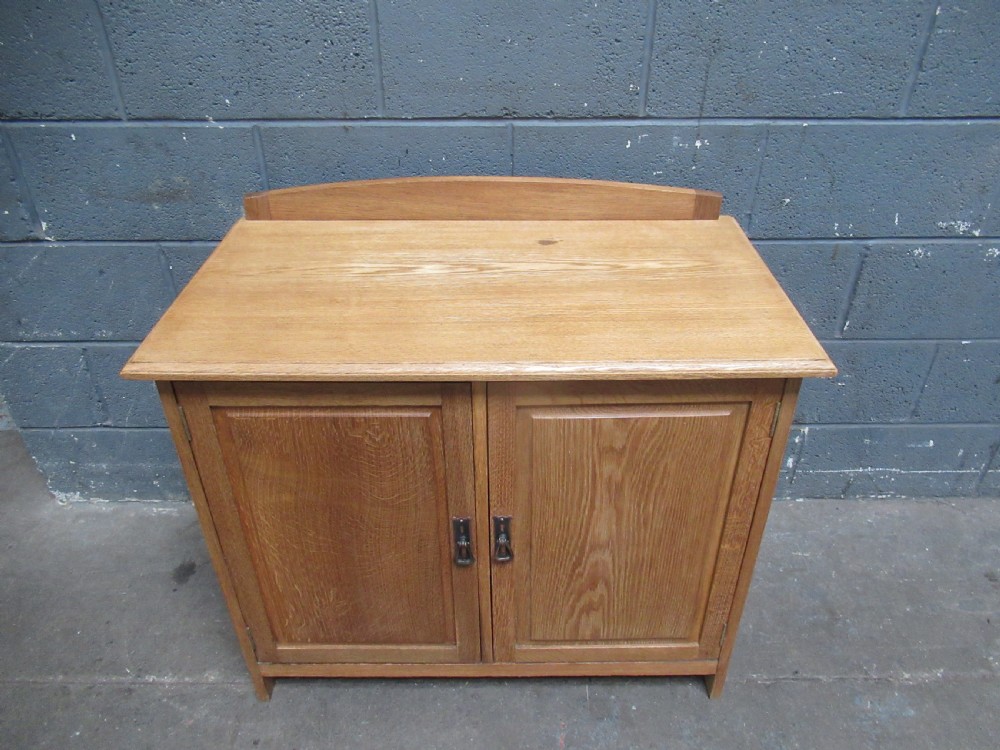 A light oak two-door storage cupboard featuring panelled doors, drop handles, and a low curved upstand along the top rear edge. View V