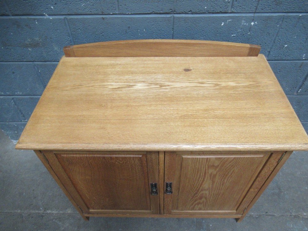 A light oak two-door storage cupboard featuring panelled doors, drop handles, and a low curved upstand along the top rear edge. View VI