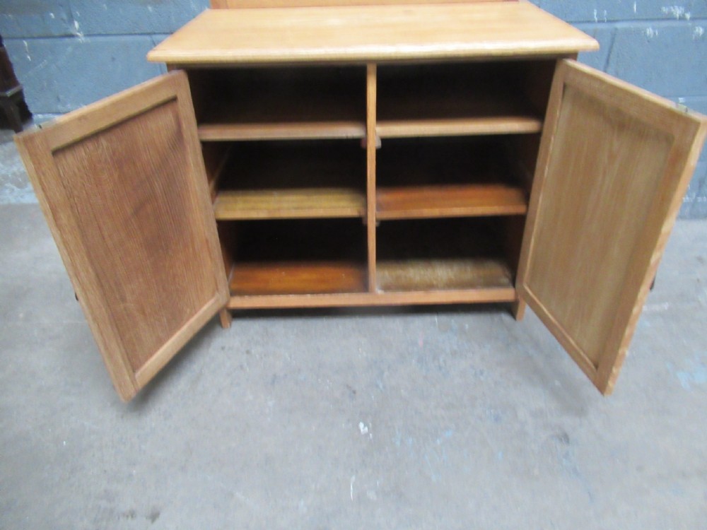 A light oak two-door storage cupboard featuring panelled doors, drop handles, and a low curved upstand along the top rear edge. View VII