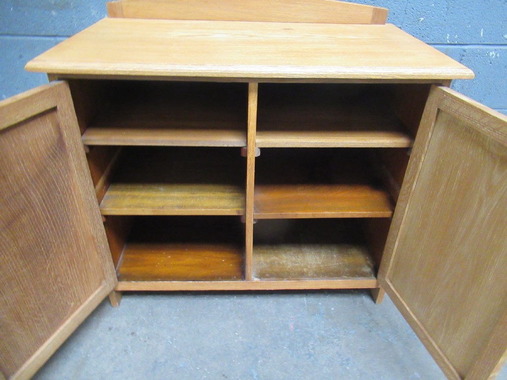 A light oak two-door storage cupboard featuring panelled doors, drop handles, and a low curved upstand along the top rear edge. View VIII