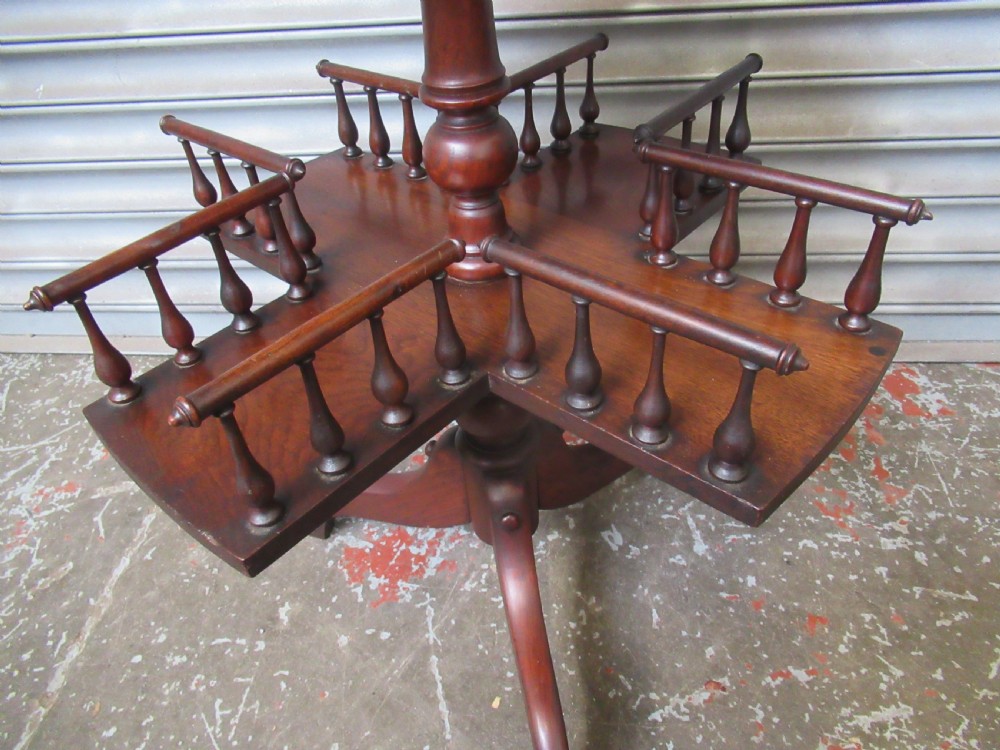 A late Victorian dark mahogany revolving book stand featuring a circular top, turned central column, spindle-galleried compartments, and a tripod base. View II