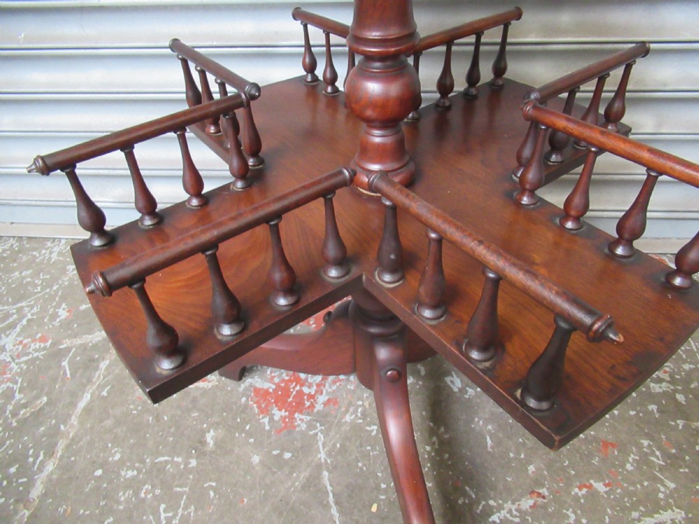 A late Victorian dark mahogany revolving book stand featuring a circular top, turned central column, spindle-galleried compartments, and a tripod base. View X