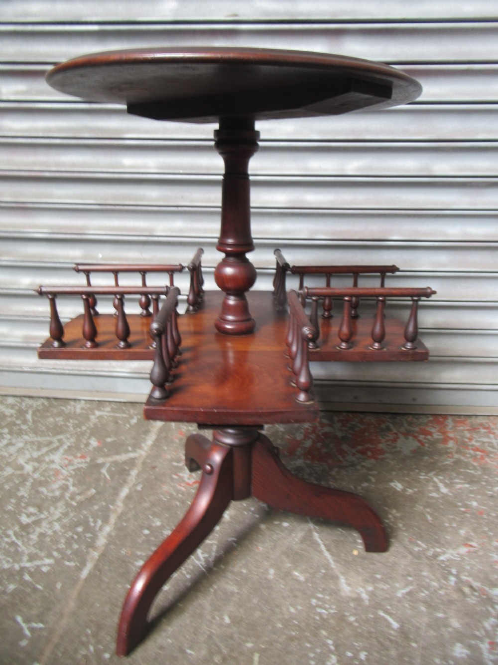 A late Victorian dark mahogany revolving book stand featuring a circular top, turned central column, spindle-galleried compartments, and a tripod base.