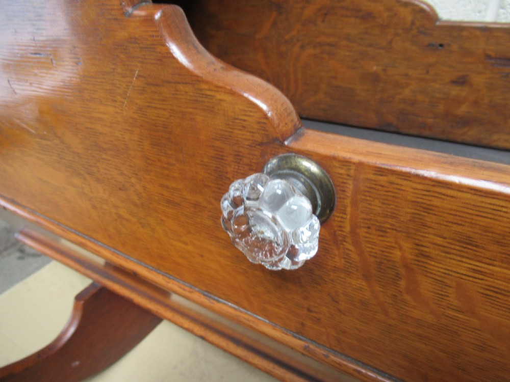 An antique Victorian oak rocking cradle with a hooded top, scalloped side rails, glass knob accent, and curved wooden rockers. View II