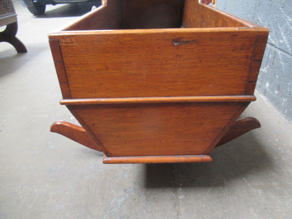 An antique Victorian oak rocking cradle with a hooded top, scalloped side rails, glass knob accent, and curved wooden rockers. View IV