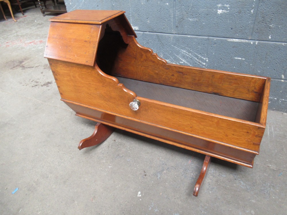 An antique Victorian oak rocking cradle with a hooded top, scalloped side rails, glass knob accent, and curved wooden rockers. View V
