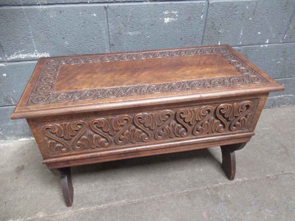 A late Victorian carved oak lidded box featuring relief foliate scrollwork on the front panel and raised on carved side supports. View II