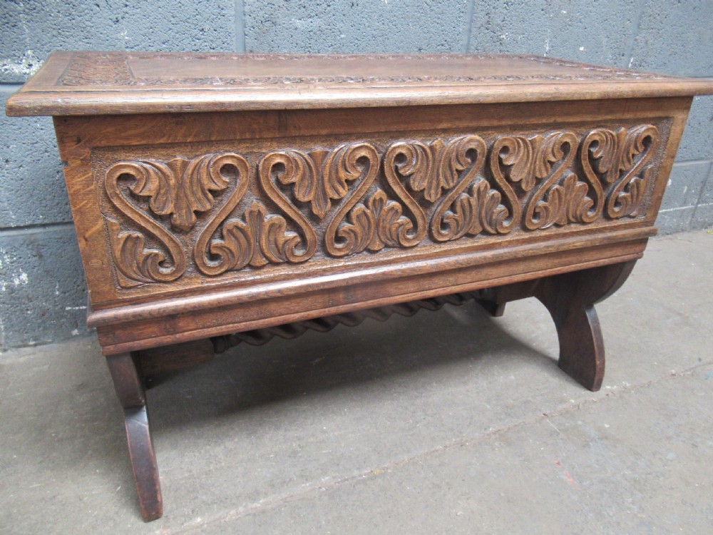 A late Victorian carved oak lidded box featuring relief foliate scrollwork on the front panel and raised on carved side supports. View III