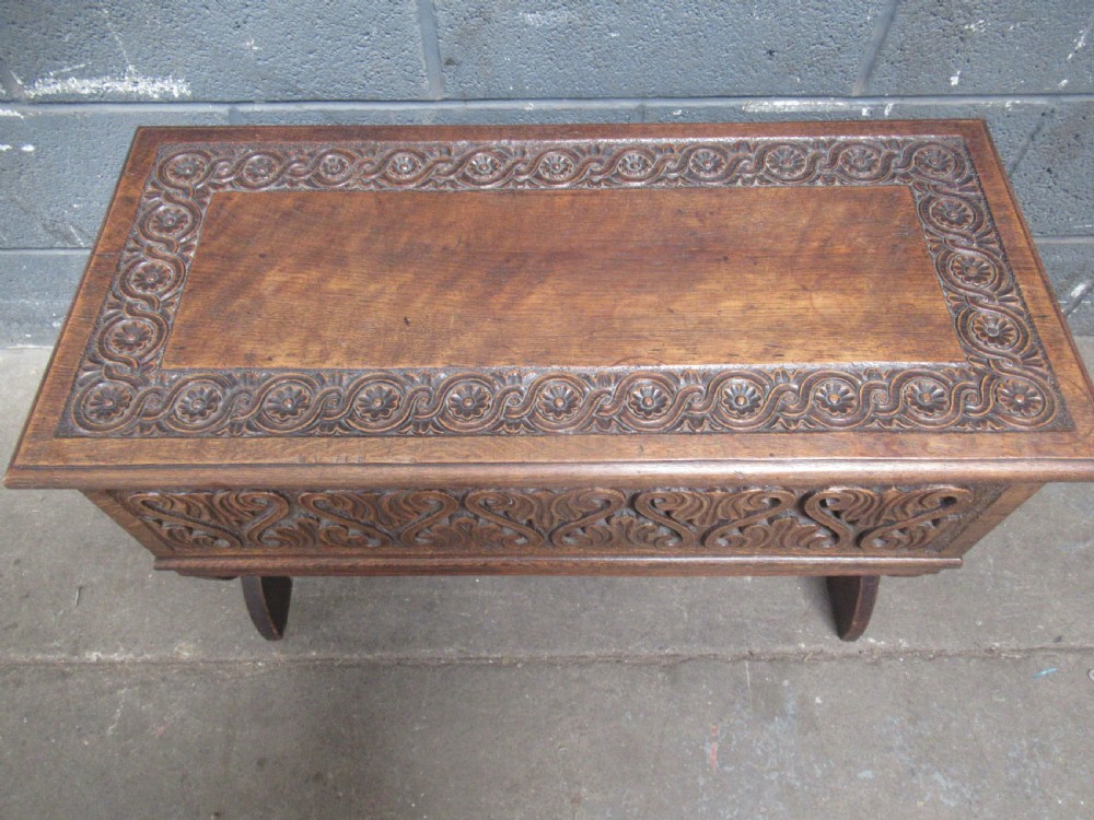 A late Victorian carved oak lidded box featuring relief foliate scrollwork on the front panel and raised on carved side supports. View IV