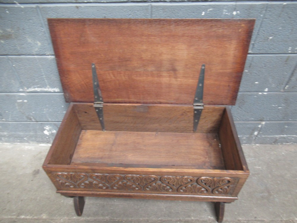A late Victorian carved oak lidded box featuring relief foliate scrollwork on the front panel and raised on carved side supports. View VII