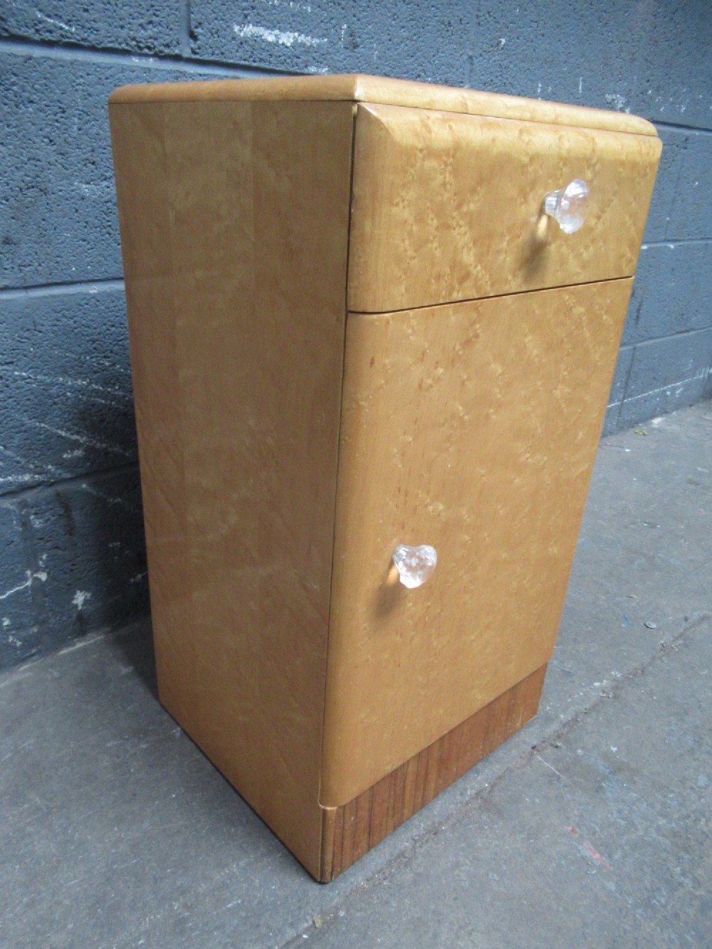 An Art Deco birds eye maple bedside cabinet with a rounded top, faceted glass knobs, single drawer, cupboard door, and darker wood plinth base. View III