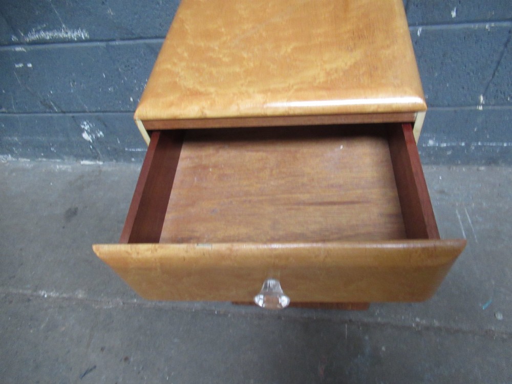 An Art Deco birds eye maple bedside cabinet with a rounded top, faceted glass knobs, single drawer, cupboard door, and darker wood plinth base. View VI