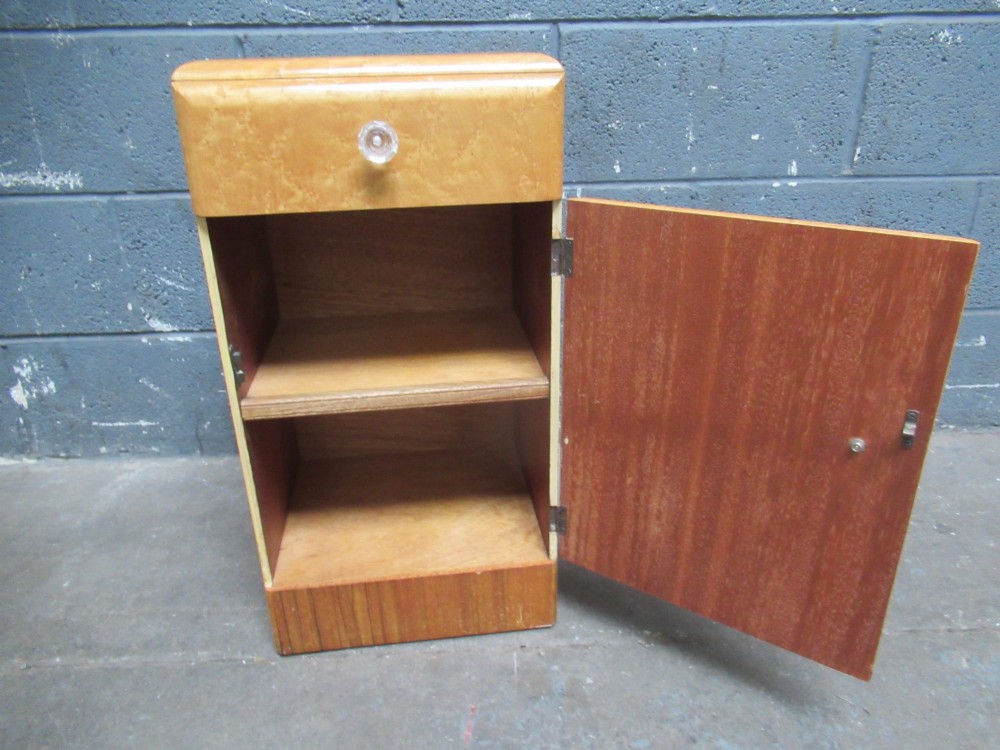 An Art Deco birds eye maple bedside cabinet with a rounded top, faceted glass knobs, single drawer, cupboard door, and darker wood plinth base. View VII