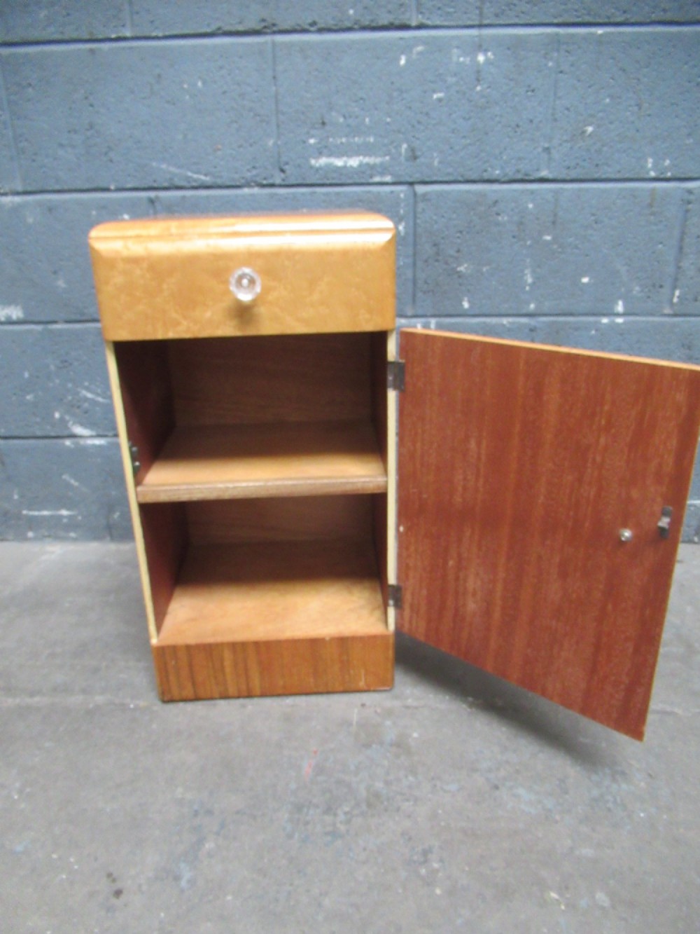 An Art Deco birds eye maple bedside cabinet with a rounded top, faceted glass knobs, single drawer, cupboard door, and darker wood plinth base. View VIII