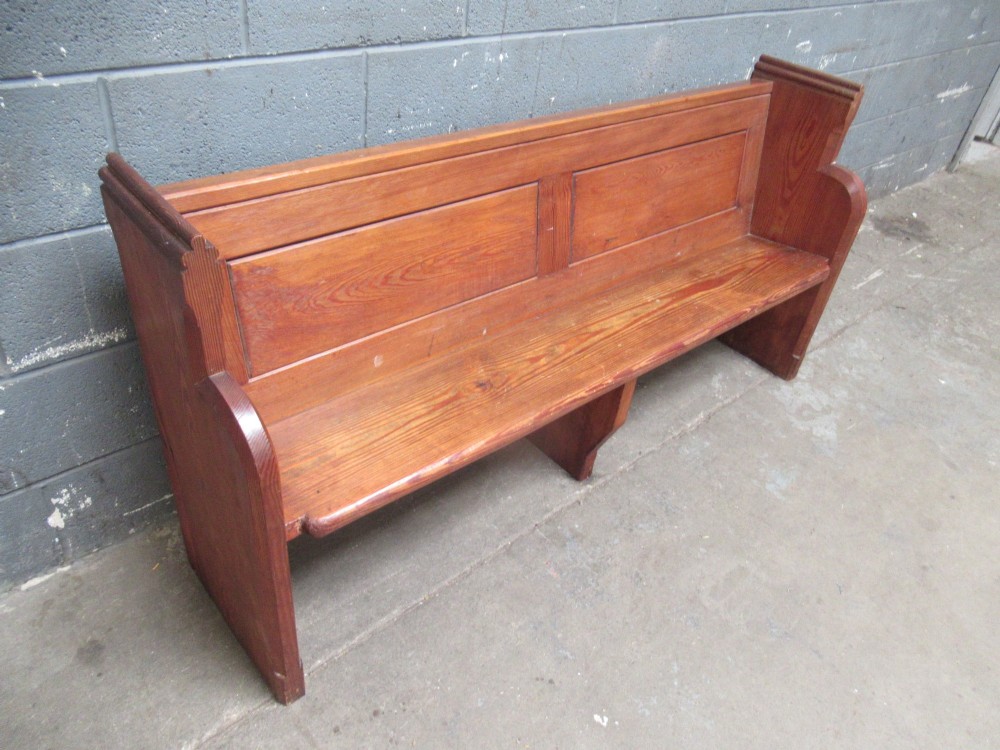 A long Victorian pitch pine church pew bench featuring a panelled back rest and carved end supports.