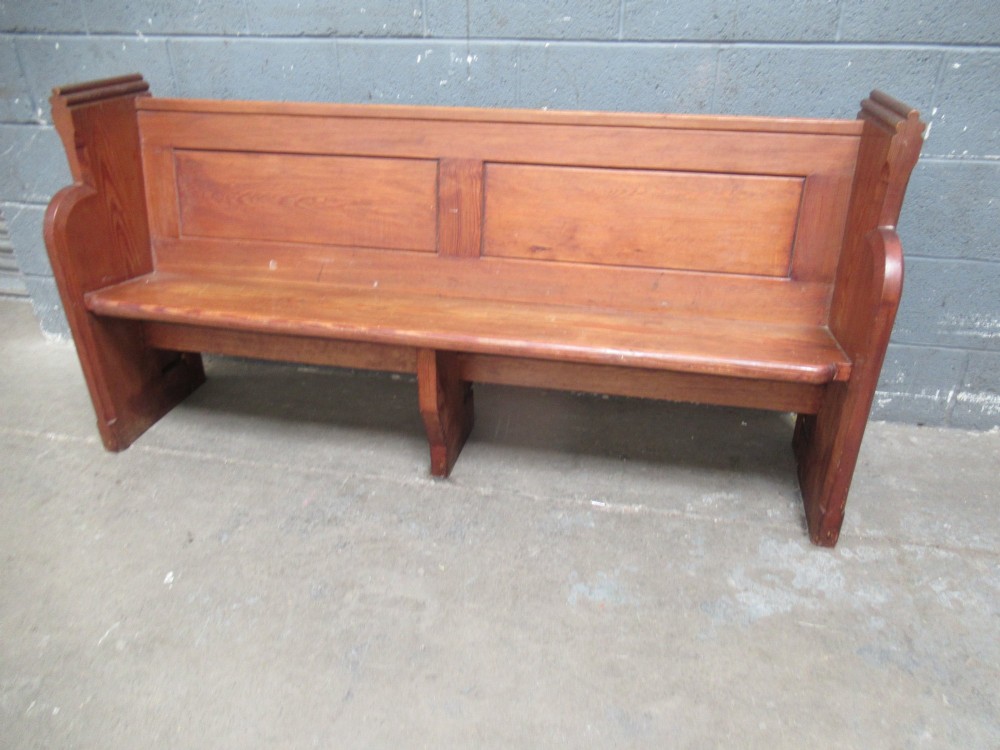 A long Victorian pitch pine church pew bench featuring a panelled back rest and carved end supports. View II