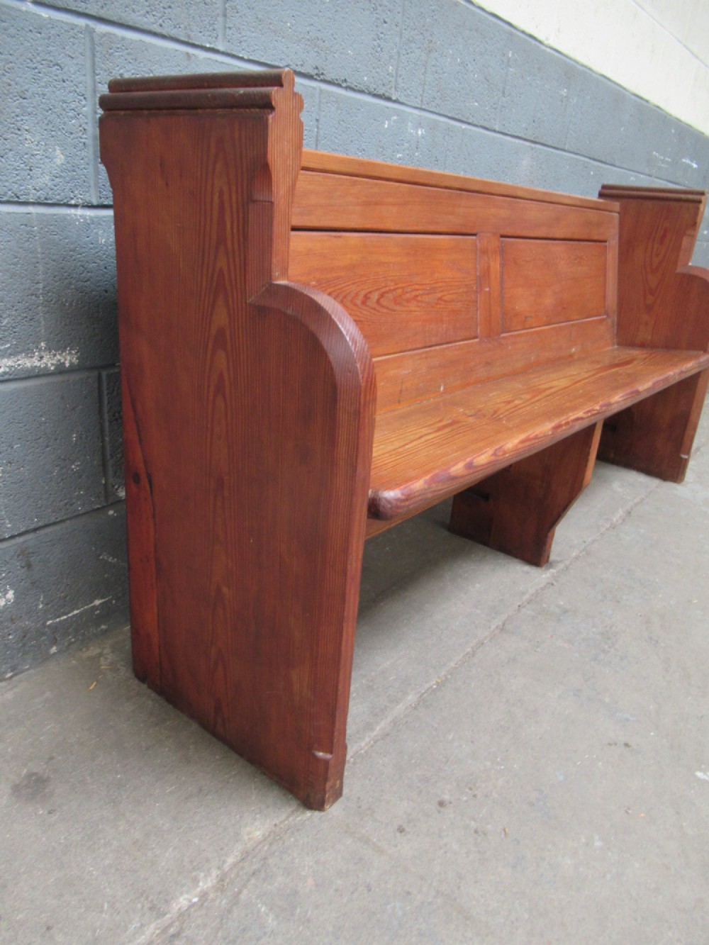 A long Victorian pitch pine church pew bench featuring a panelled back rest and carved end supports. View III