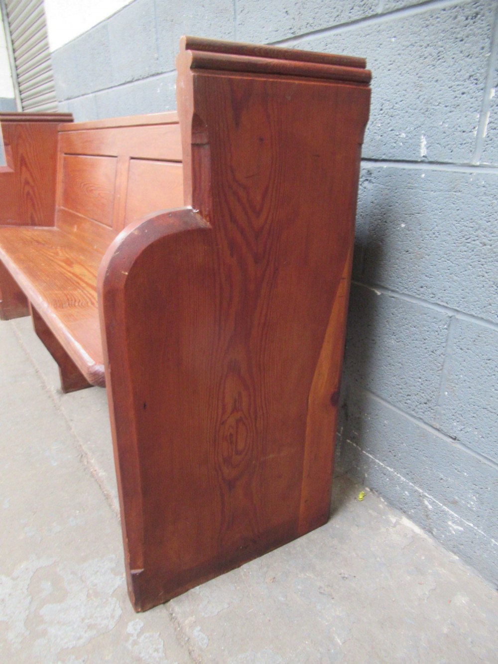 A long Victorian pitch pine church pew bench featuring a panelled back rest and carved end supports. View IV