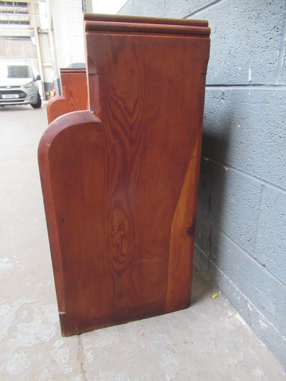 A long Victorian pitch pine church pew bench featuring a panelled back rest and carved end supports. View V