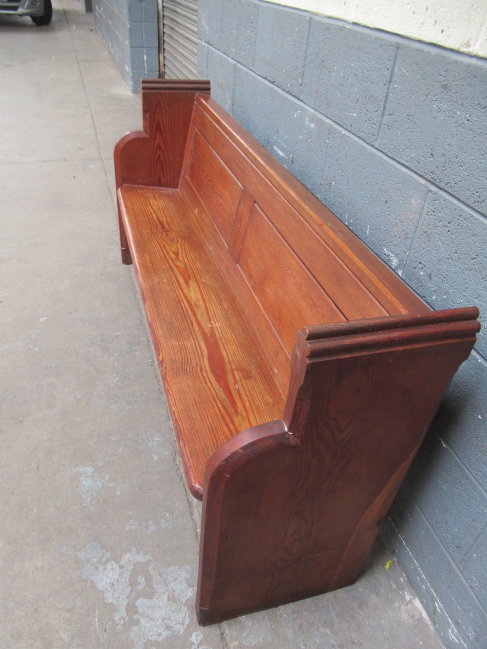 A long Victorian pitch pine church pew bench featuring a panelled back rest and carved end supports. View VI