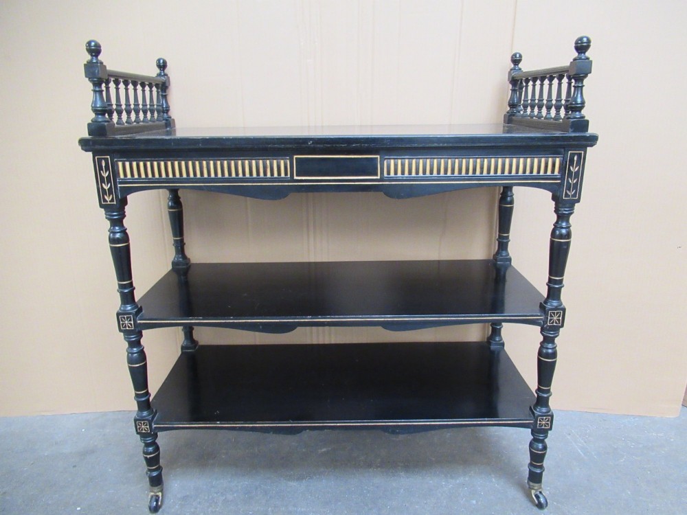 Victorian ebonised three-tier side table featuring spindle side galleries, turned legs, brass castors, and gold fluted detailing on the frieze.